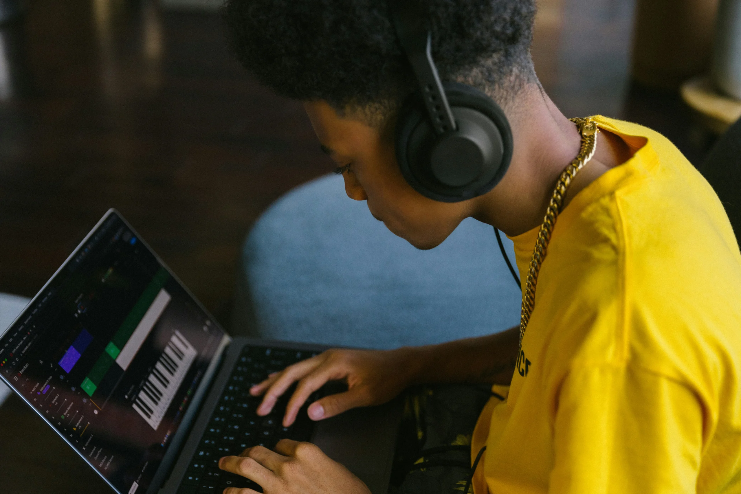 Person in gelbem T-Shirt mit Kopfhörern arbeitet am Laptop mit Musiksoftware
