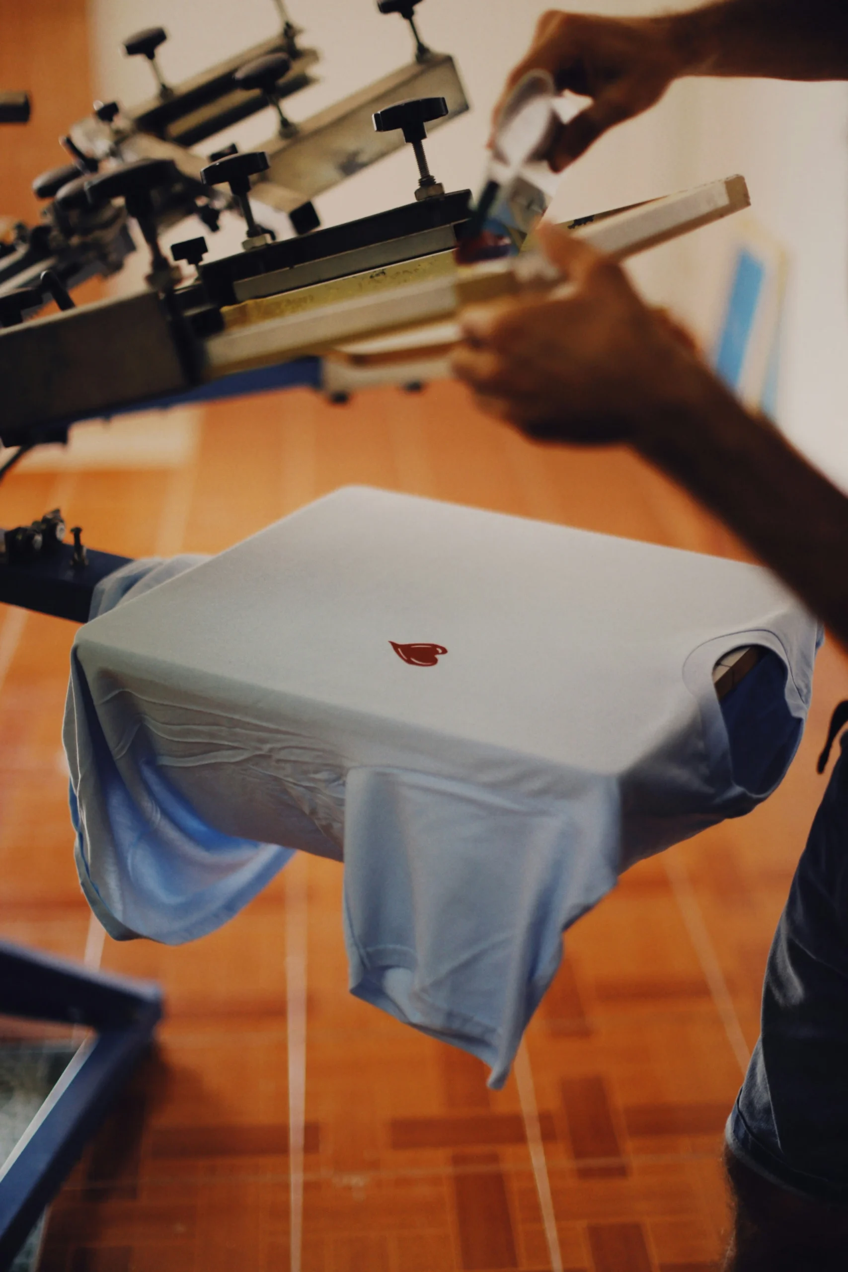 Ein T-Shirt liegt auf einer Druckplatte, während eine Person Farbe für den Druck aufträgt
